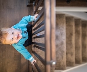 toddler standing behind a baby gate at the top of the stairs